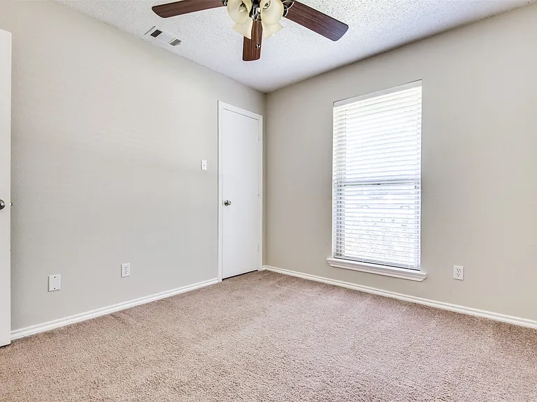 Carpeted room featuring a ceiling fan with light fixture, a window with horizontal blinds, and light-toned wall paint