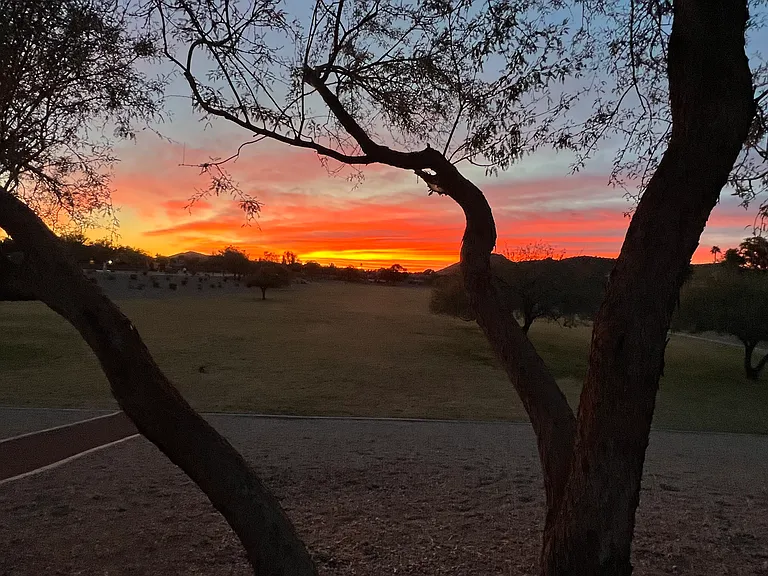 view of sunset from sand playground by the enormous grass park and paved walking path that goes all the way around in a loop