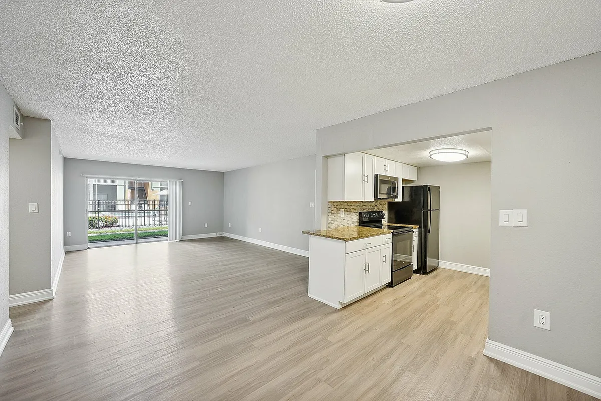 Spacious living room with elegant wood flooring and modern kitchen featuring sleek appliances and granite countertops. - River Rock Apartments