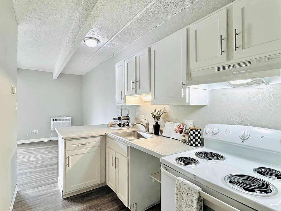 Modern kitchen with sleek white cabinets, modern appliances, and a stylish countertop, leading into an inviting living area with natural light.