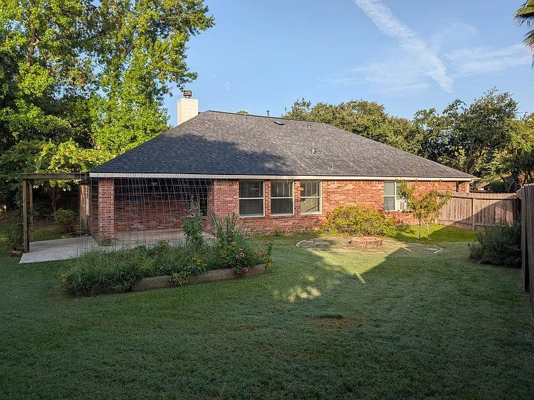 Highlighting the all-brick rear exterior, established garden beds, and the sheer depth of this oversized lot.