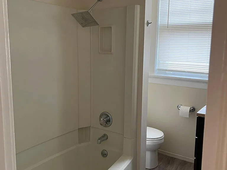Bathroom view 2 shows tub/shower, wall sectioned toilet area, storage above tub area, and new tiled floor matching kitchen.