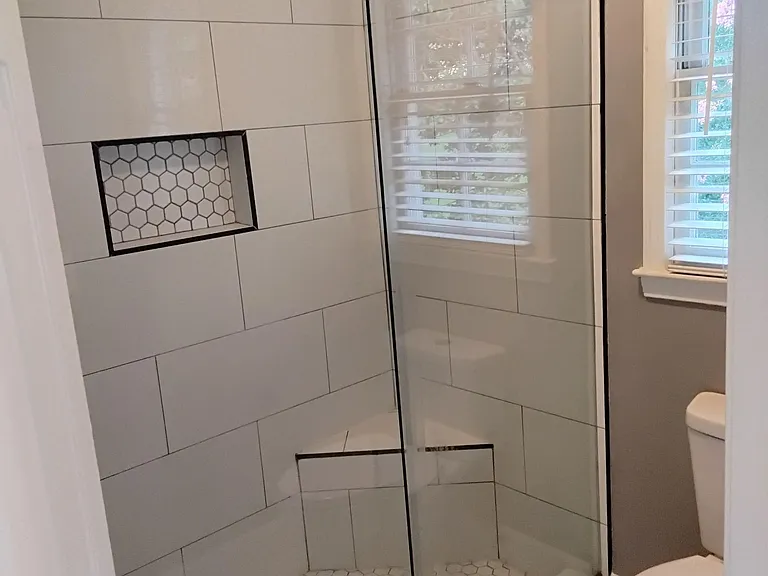 Tiled walk-in shower with frameless glass, built-in niche, and window for natural light in a well-appointed bath.