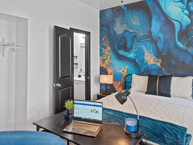Furnished bedroom with a work desk, accent wall, and convenient access to an en-suite vanity and storage closet.