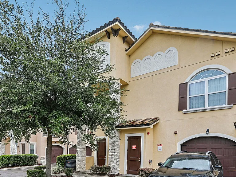 Charming townhouse exterior with a Mediterranean design, featuring stucco walls, arched windows, and a welcoming driveway.