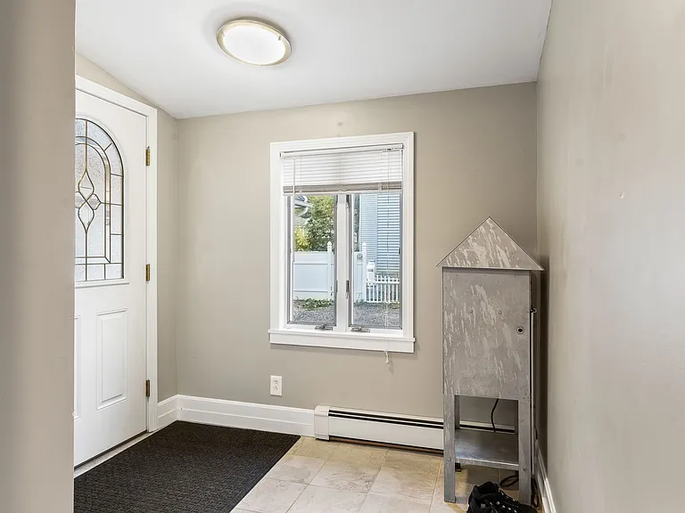 Front door entrance showing natural light from the window, baseboard heating, and ceiling light fixture.