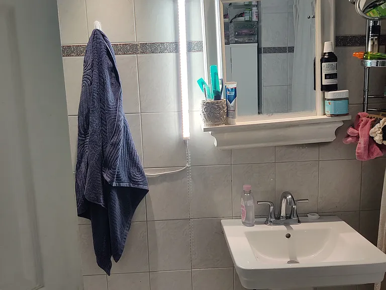 Spacious fully tiled bath with ceramic pedestal sink.