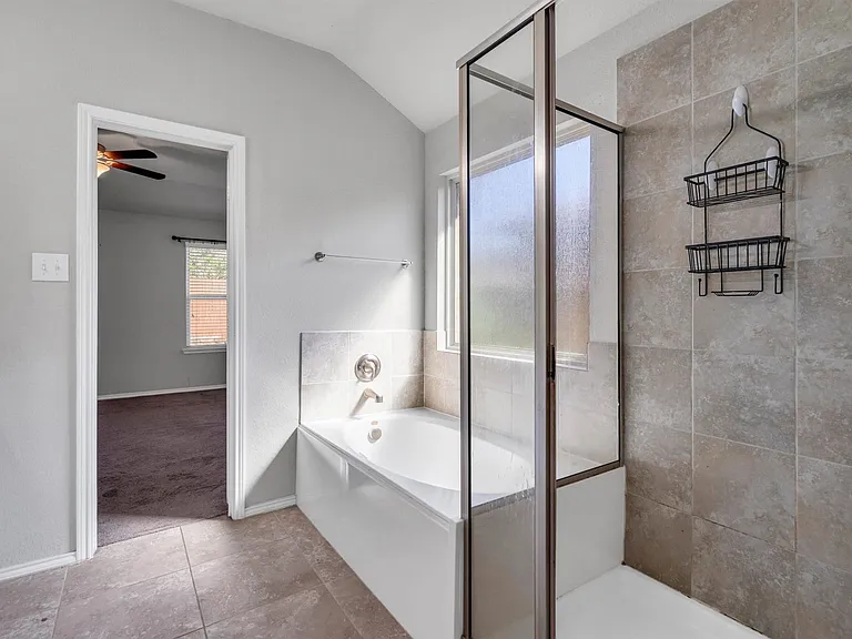 Bathroom featuring a built-in tub with a glass panel shower enclosure, light-toned wall tiling, coordinating floor tiles, and a window providing natural light