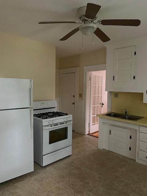 Kitchen showing a small portion of cabinets, other wall has two windows. Closed door is entrance to apartment; french-door leading to a living room with one window and a door leading to a private porch.