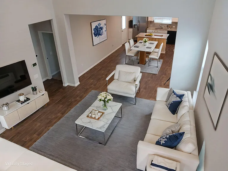 Staged Living room displays the open floor plan that connects to the dinning room and modern kitchen in the background. Entryway to the left leads to the primary bedroom