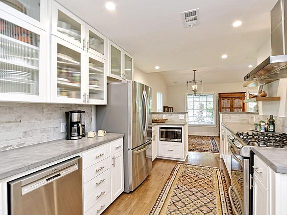 Recent kitchen with white cabinets, concrete counter tops, SS appliances including a gas range.