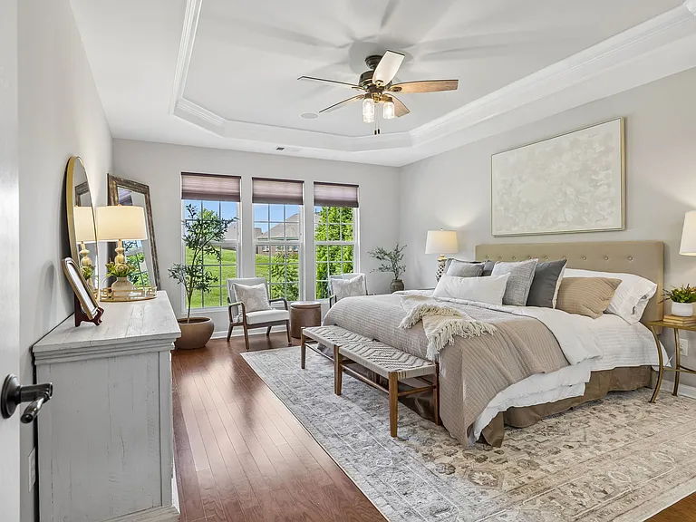The spacious main-level primary suite serves as a private retreat, featuring a tray ceiling, hardwood floors, abundant natural light & a cozy sitting area overlooking the beautifully landscaped property.