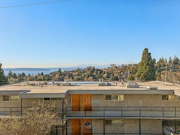Experience stunning panoramic views from 4400 Alaska apartments in Seattle, WA. This exterior shot showcases Puget Sound, hills, and majestic Olympic Mountains.