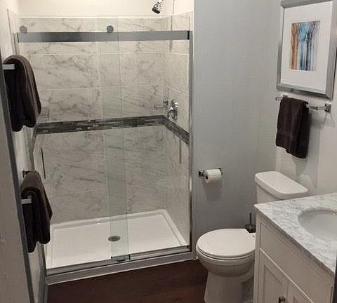 Bathroom with glass enclosed shower, hardwood floor and marble topped two-sink vanity