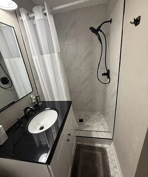 Compact bathroom featuring a single-sink vanity, framed mirror, and walk-in shower with tile surround and curtain.