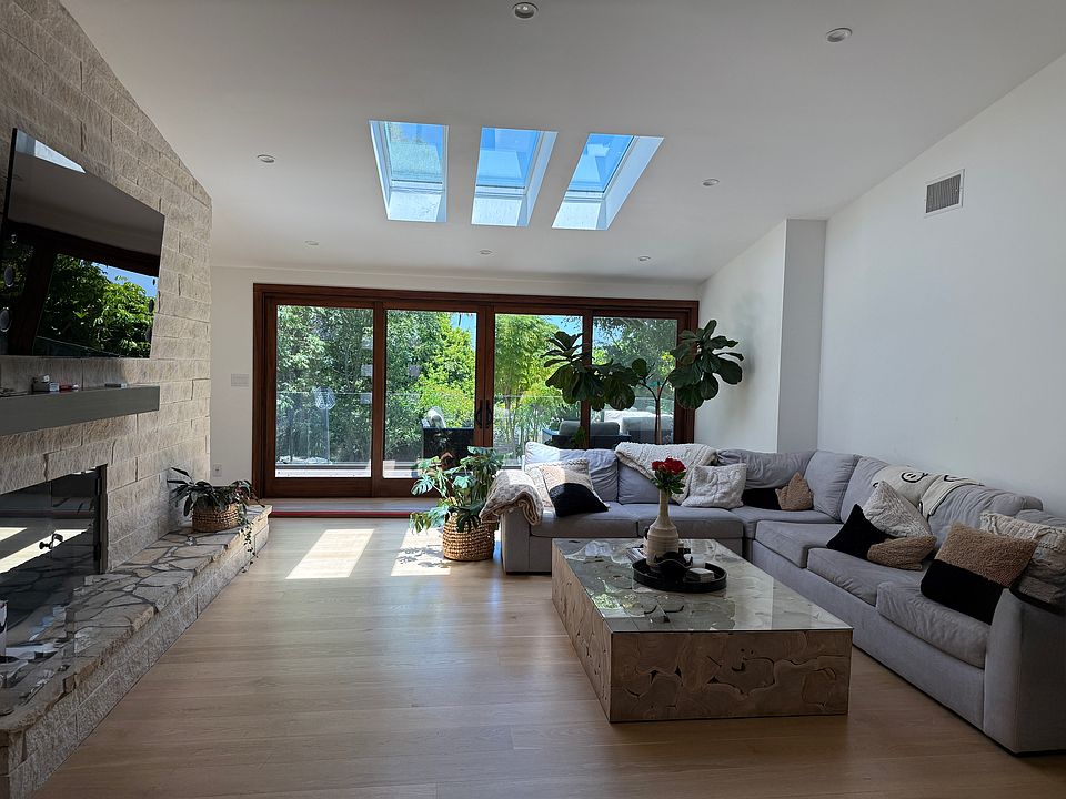 Upon entry, you're welcomed into a spacious dining and living area, divided by a dual-sided fireplace. Natural light pours in through remote-controlled skylights and double-pane sliding glass doors that lead to a deck with a lush landscaped yard.