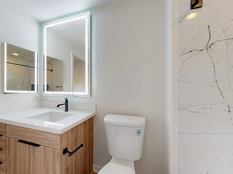 Apartment bathroom with wood-style flooring and LED vanity mirror.