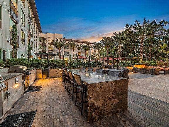 Expansive social courtyard featuring bocce ball and ping pong, fire pits surrounded by intimate seating areas, and grills with open-air dining areas