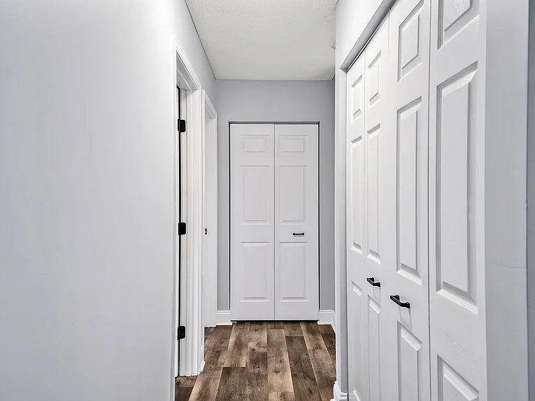 View of the hallway from the living room. Laundry room folding doors to the right, 2 bedroom doors to the left, linen closet straight ahead, and master bedroom down the hall to the right