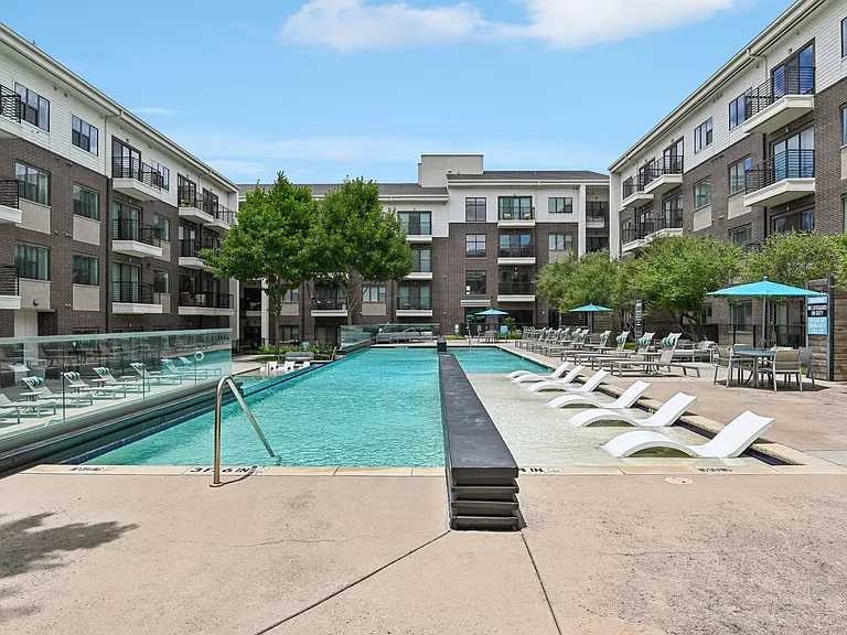 Markethaus 3700 A large swimming pool surrounded by lounge chairs and umbrellas in front of apartment buildings.
