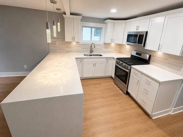 Spacious kitchen with a large quartz island, ample white cabinetry, tile backsplash, and stainless gas range.