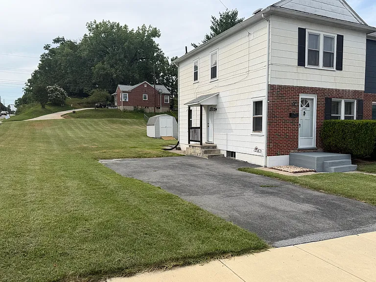 Side view of house showing side entrance into kitchen, plenty of off-street parking in large driveway for 2+ vehicles, big yard with shed.