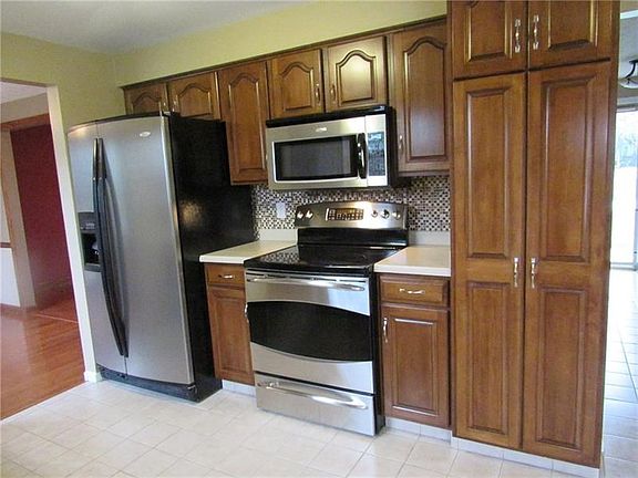 Kitchen with tiled backsplash, solid surface counter tops, stainless steel appliances, & neutral tiled flooring