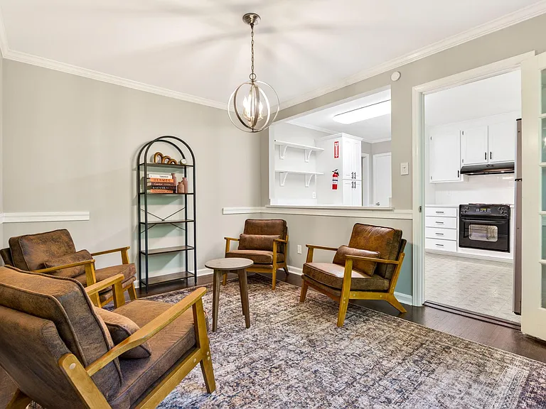 Shared living area with lounge seating, area rug, and overhead pendant lighting, opening to the kitchen for easy flow.