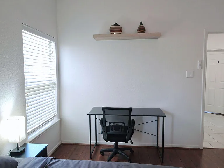 Bedroom with a furnished work desk, window with blinds, and ample wall space for storage or decor.