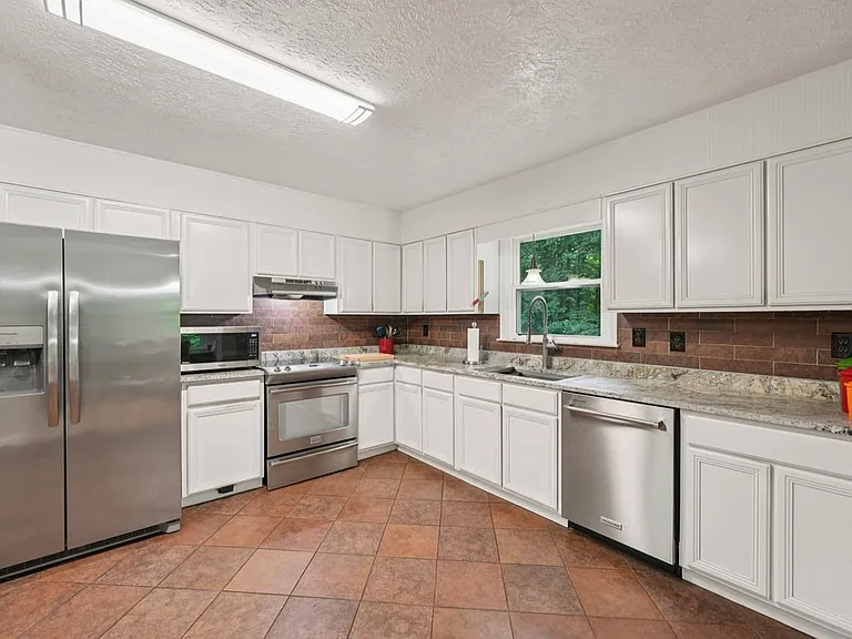 This charming kitchen blends practical elegance with storybook warmth, offering generous cabinet space, polished countertops, and a peaceful window view into the greenery beyond.