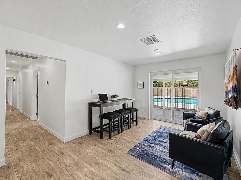 Open common area with lounge seating, bar-height workspace, and sliding doors to a covered patio and pool view.