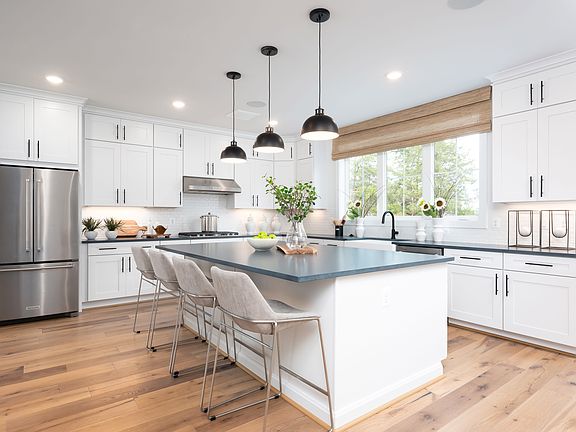 A modern, bright kitchen with white cabinets, a large island with stools, and pendant lighting over