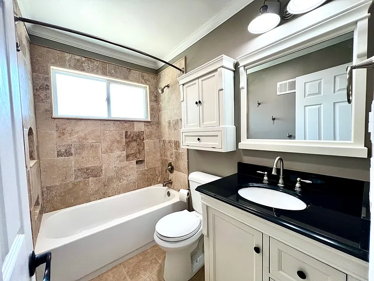 Full bath with extra storage and travertine tile. Tall shower head, easy clean fixtures, and full linen closet in hall.