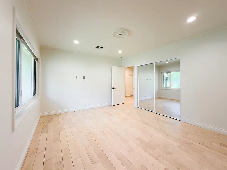 Mirrored closet doors reflect natural light in this spacious unfurnished bedroom, a comfortable option in a Beverly Hills luxury rental at 1094 Garden Lane, 90210.