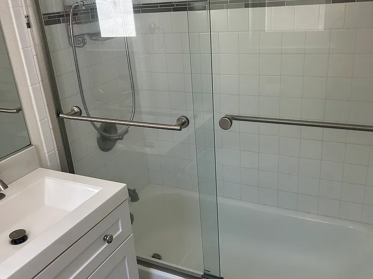 Shower / Bath Combo with glass doors, and a built-in exhaust fan in the ceiling.