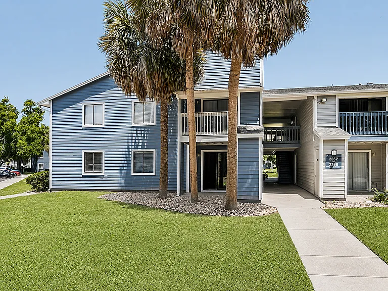 Charming blue apartment building with lush green lawn and elegant palm trees, offering a welcoming and serene living environment.