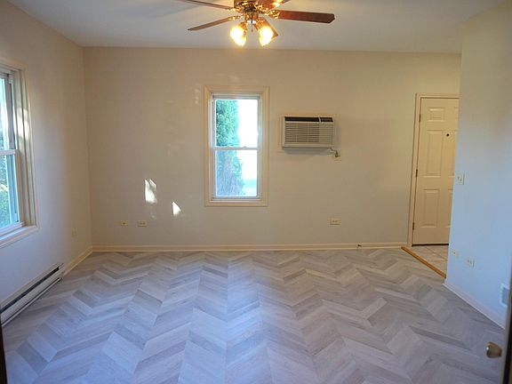 Spacious living room with new flooring, ceiling fan, and wall fit air conditioner.
