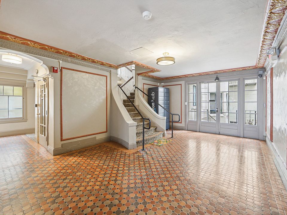 Hallway is illuminated by a chandelier hanging from the ceiling, and a window on the far left side allows natural light to enter the room
