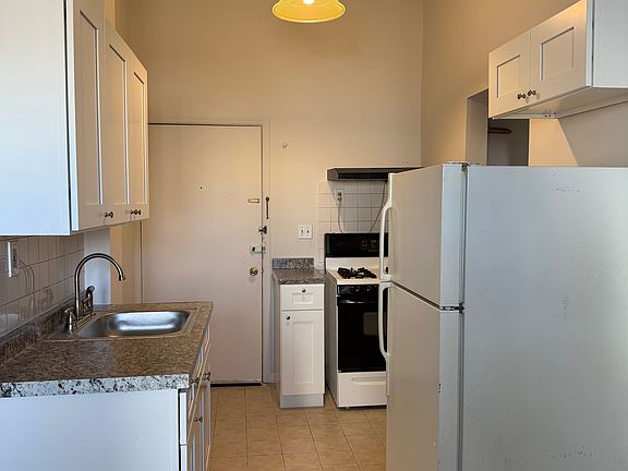 Kitchen with new cabinets and refrigerator. Tall ceiling with drop lighting.