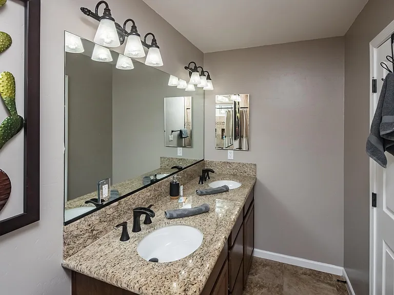 Spacious bathroom with dual sinks, granite countertops, large mirror, and upgraded lighting.