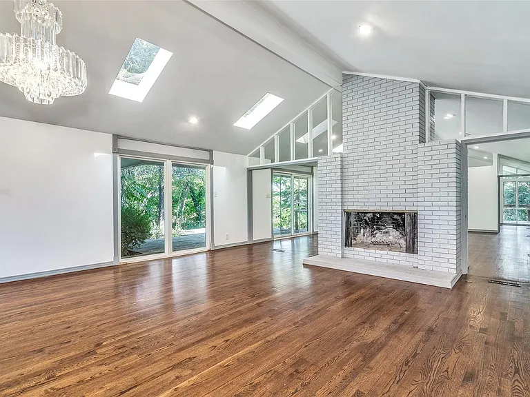 Spacious room featuring wood-finish flooring, a white-painted brick fireplace with a stone hearth, and a vaulted ceiling with skylights