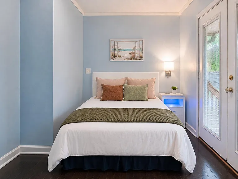 Private bedroom with a full bed, nightstand lighting, and French doors with blinds providing easy outdoor access.