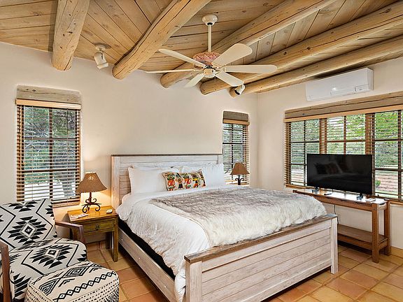 Primary bedroom with a king bed, reading chair with ottoman, tall ceilings, lots of windows, and a ceiling fan.