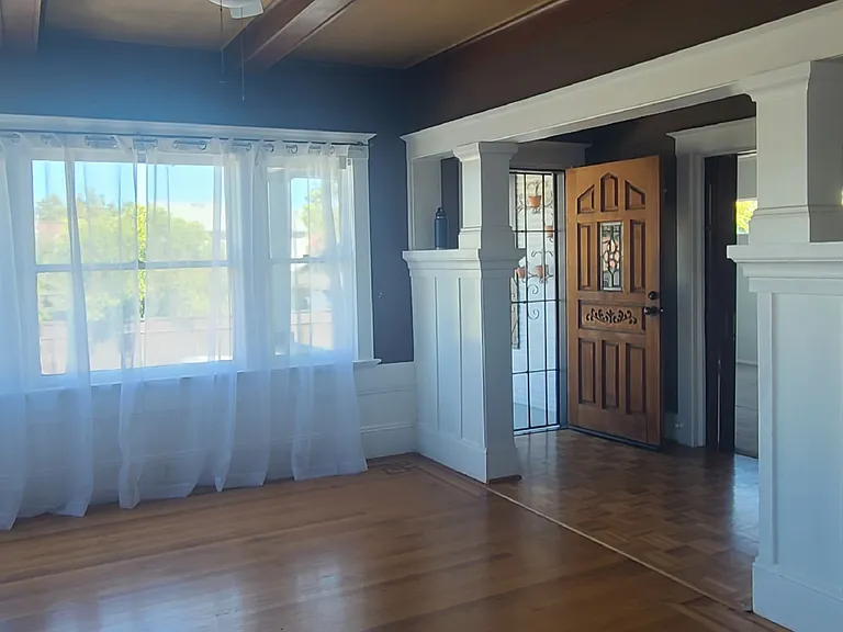 A view from the dining room into the formal living room and the front entry. Original hardwood floors with hand laid wood work details.