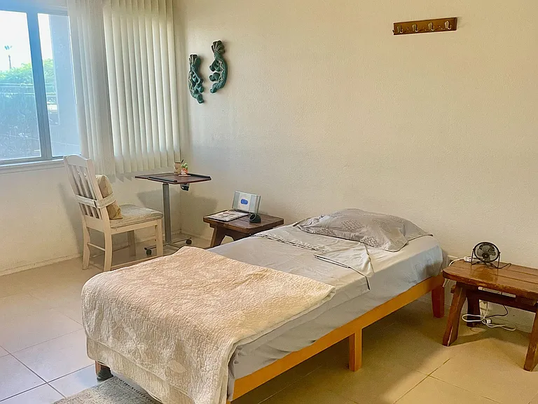 Furnished bedroom with a twin bed, desk setup, and large window with vertical blinds for comfortable everyday living.