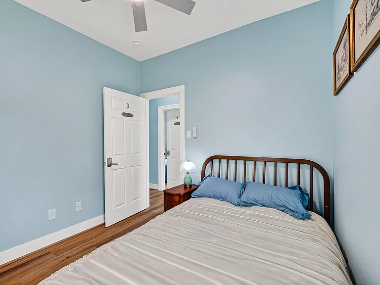Private bedroom with a full bed, ceiling fan, wood-look flooring, and convenient nightstand lighting with easy hallway access