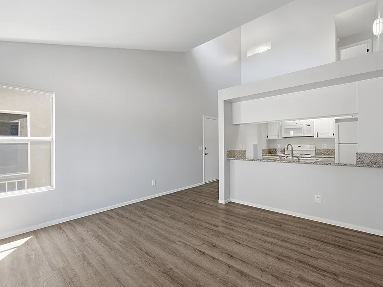A large empty room with wooden floors and a kitchen area in the background.