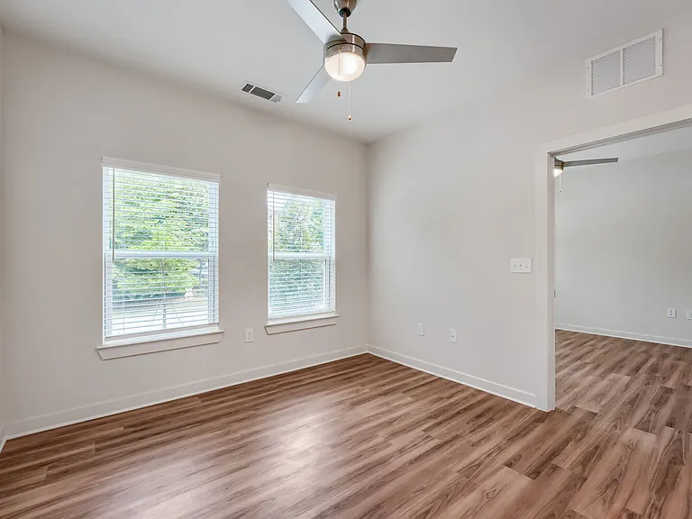 Bedroom with windows and ceiling fan and door leading to living room