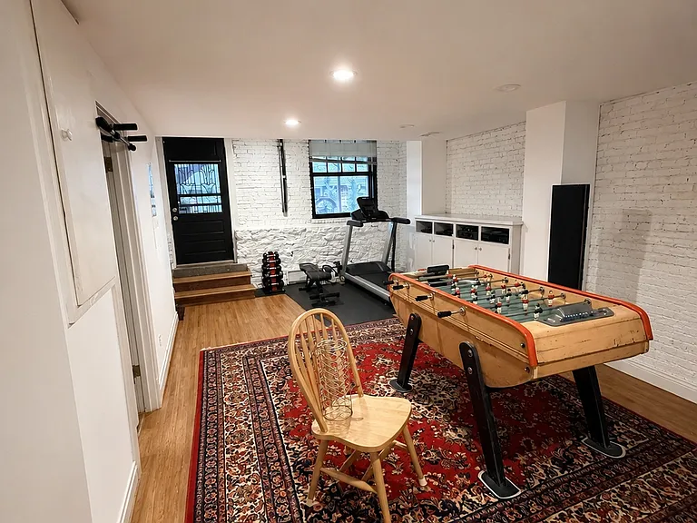 Basement recreation area with foosball table, exercise equipment, and exposed brick detail.