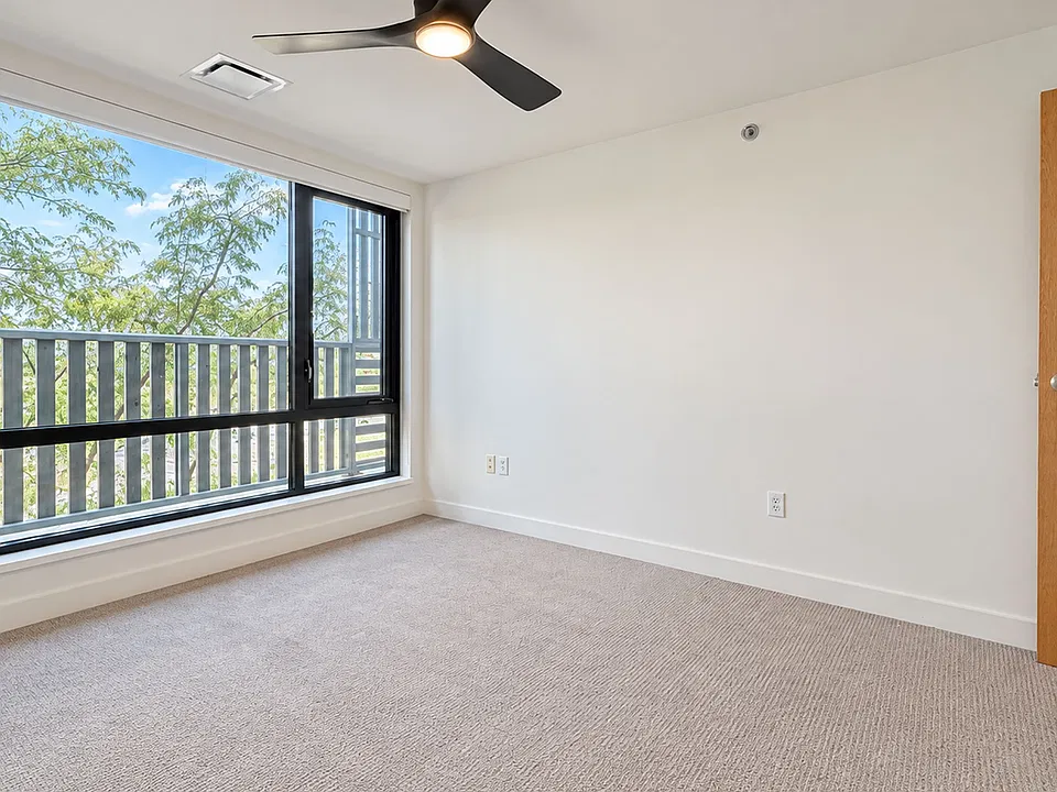 Brighten your day in this airy Farmers Park Apartments home, featuring large windows, soft carpeting, a ceiling fan, and a private balcony. Explore available apartments today!